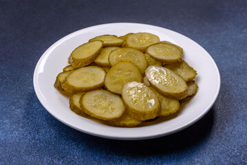 Delicious salted, canned cucumbers cut into slices on a white ceramic plate