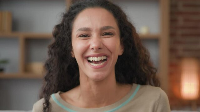 Headshot portrait closeup indoors happy female face cheerful Hispanic woman with curly hair feels good mood happy laughs over humor joke funny comedy having fun enjoy moment laughing with dental smile