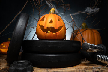 Small ceramic Halloween pumpkin on a dumbbell barbell weight plates. Healthy gym fitness lifestyle...
