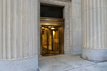 Building entrance, with brass revolving door in between large stone columns