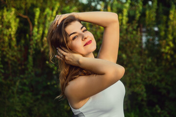 Naklejka premium Young woman touches her hair in the garden at sunset .in a white shirt