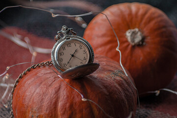 Vintage retro pocket watch with long chain near autumn orange holliday pumpkins on a checkered...