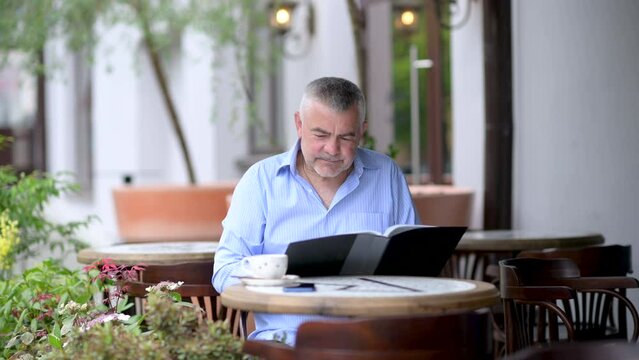 Handsome caucasian middle aged man hoosing lunch menu in street cafe.	
