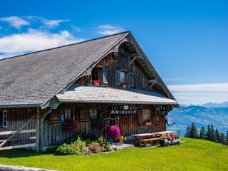 A beautiful wooden cottage on a mountain meadow in Switzerland with flowers in the windows