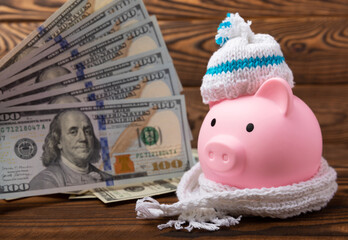 Savings concept. Piggy bank and money on a brown wooden table. Piggy bank in a warm winter hat and scarf, heat saving. Saving heating concept.Place for text. Copy space