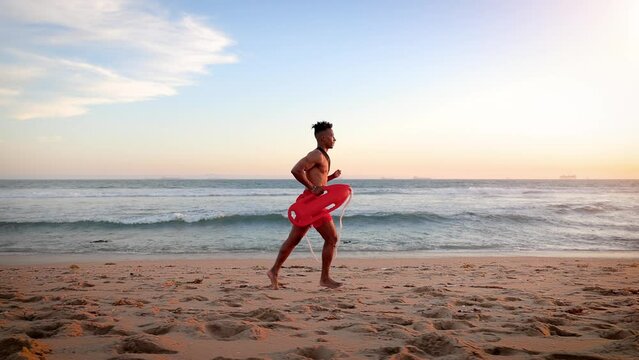 African American lifeguard running along the beach in Southern California at Sunset. Lifeguard's left hand is deformed.