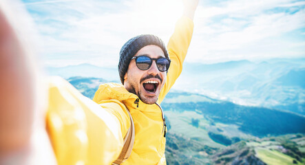 Handsome man taking selfie picture on top of mountains - Happy hiker smiling at camera trekking...