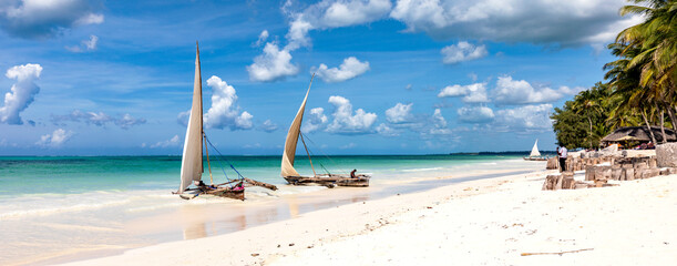 Traditionelle Dhows an einem Strand auf Sansibar. Boote im türkisfarbenes Ozean und blauer Himmel in Tansania, Panorama. - obrazy, fototapety, plakaty