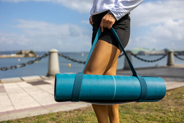 Rolled up yoga mat with a belt in the hands of a girl
