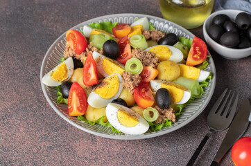 French salad Nicoise with tuna, boiled potatoes, egg, black olives, cucumbers, tomatoes and lettuce on brown background