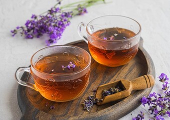 Lavender tea in transparent glass cups on a wooden tray on a light concrete background. Hot drinks.