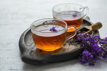 Lavender tea in transparent glass cups on a wooden tray on a light concrete background. Hot drinks.