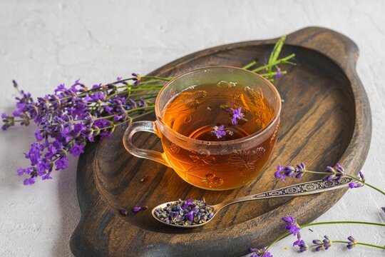 Lavender tea in transparent glass cups on a wooden tray on a light concrete background. Hot drinks.