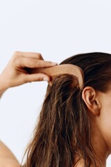 Naklejka premium A woman with long brown hair stands back and takes care of her hair after washing and combing her hair with a wooden comb. Healthy hair without hair loss