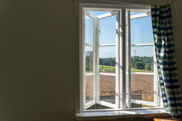 View from open window in the village. White old wooden windows with view on blue sky and green field. Symbol of insouciance, freedom, summer atmosphere. Holiday house, summer cottage, weekend cottage.