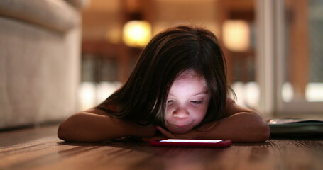 Child watching cellphone screen at night. Blue light from smartphone device glowing on little girl...