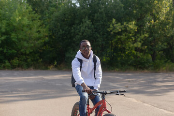 A smiling African-American man rides a bicycle through a public park. Sports and recreation