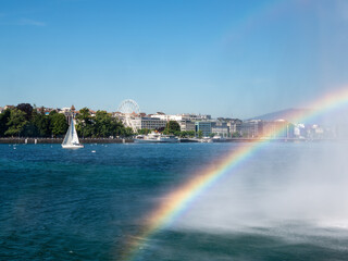 Geneva, Switzerland - July 13, 2022: Rainbow from water jet over Lake Geneva and view of the city of Geneva