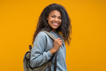 Portrait of cute smiling african american girl student posing with a backpack isolated over bright...