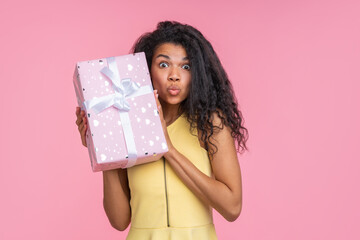 Studio portrait of cute coquette young woman posing with decorated present box in hands isolated over pastel pink background