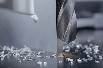 metal drill bit make holes in steel billet on industrial drilling machine with shavings. Metal work...