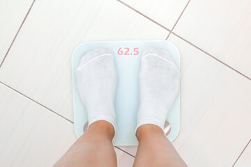 A woman feet in white socks are on an electronic scale in the bathroom, she is overweight and she wants to lose weight
