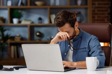 Handsome male businessman manager working tiredly behind a laptop in a stylish home office. Loss of...