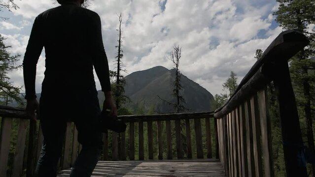 Slowmo Of Rear View Of An Asian Man With Camera In Hands Walking Towards Observation Deck And Taking Photo In National Park In Eastern Sayan Mountains In Summer