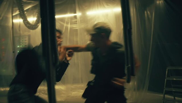 Criminal or mafia member and police officer in body armor aggressively fighting in dim basement illuminated by LED lamps. Action movie scene