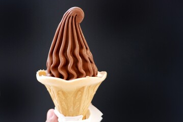 A soft cone of chocolate ice cream on a female hand with dark background 