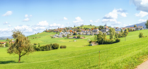 Fototapeta na wymiar Idyllic village on hill in Switzerland. Swiss summer panorama with agricultural fields, rolling hills and rural residential homes and church nested on a hilltop. Schwarzenberg, Luzern, Switzerland
