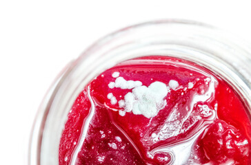 Mouldy jam in jar, top view. Bright red berry jam with white fuzzy mold spores on top in mason jar. Concept for food safety, save to scrape off and gastro illness caused by fungi. Selective focus.