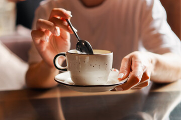 Closeup of female hands with french manicure holding cozy ceramic white mug of tea or coffee. Relax and comfort at home, cafe. Drinking hot cocoa. Empty space for text on blurry background, backplate