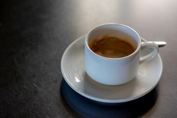 Selective focus on white coffee cup and saucer and spoon on the wooden table, Black coffee and brown creamy foam with free copy space, Outdoor drinking warm drink in the afternoon.