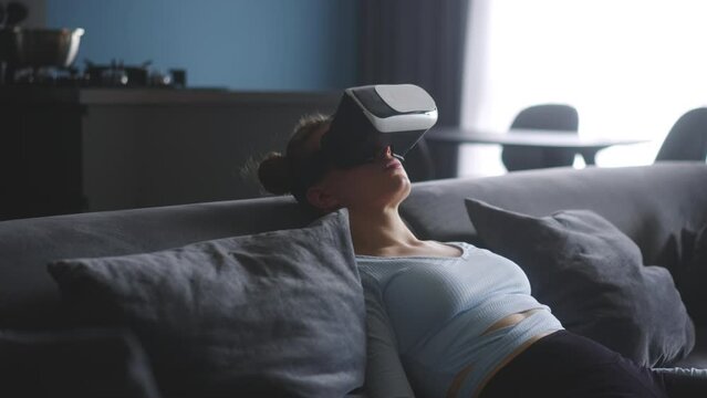 Woman in virtual reality goggles enters metaverse, controls immersive experience with hand gestures via headset interface in minimalistic interior. Girl gaming in cyber space. Futuristic concept.