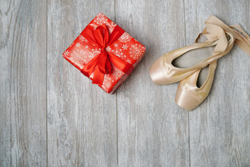 Pointe shoes and a red gift on a wooden background.