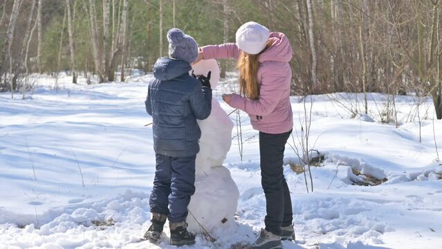 Winter fun. Happy mom and son are building a snowman in a snowy park. Lovely family at winter holidays.