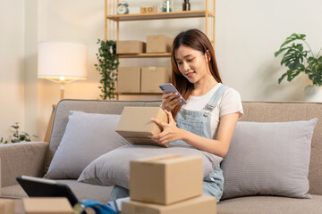 Obraz premium Young entrepreneur is holding cardboard boxes to taking a picture to sending customer while sitting