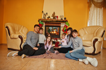Happy young large family at home by a fireplace in warm living room on winter day.