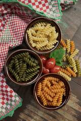 pasta, tomatoes and spinach on wooden table.  uncooked Fusilli multi-colored.