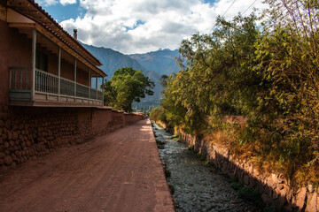 Typical adobe houses with plants next to the water canal, between mountains in the village of Urquillos. Sacred Valley, Peru. 