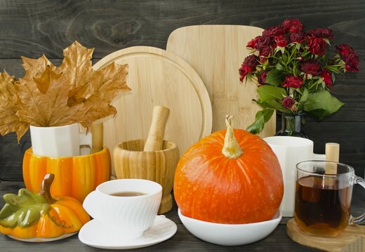 Decorative autumn composition for Halloween.  Home decor for the kitchen.  Cutting boards, cups, autumn leaves and flowers, juicy pumpkin, yellow corn, cup of tea and coffee, front view.  Close-up.
