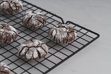 Angle view shot food photo of freshly baked Chocolate Crinkle Cookies. Chocolate iced biscuits arranged on black wire cooling rack. White work surface background. Copy space available