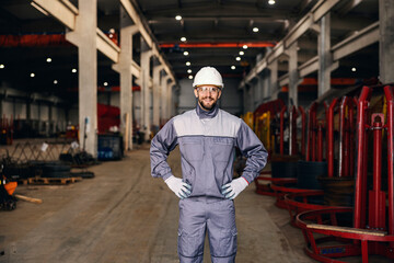 A successful factory manager in working clothes stands in the facility and smiles at the camera.