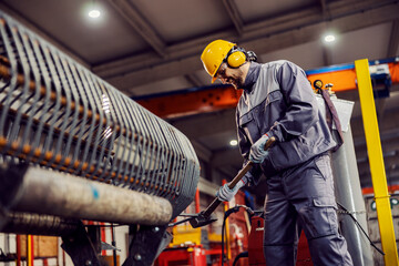 A metallurgy worker is fixing a metal framework with a hammer in the factory.