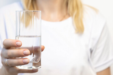Close-up of a woman holding a glass of drinking water in front of her.