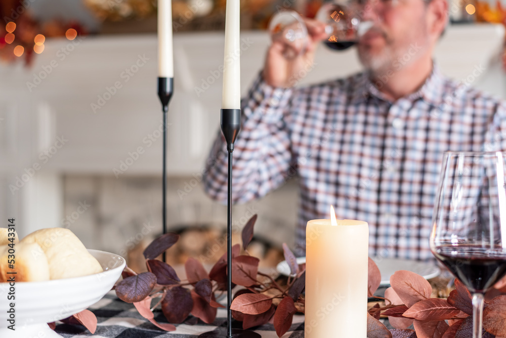 Wall mural Holiday dinner table with a man drinking wine in blurred background