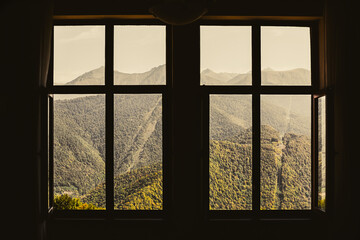 View through old open wooden window of cottage on slopes. Stunning tranquil scene in Europe. Colorful Greater Caucasus ridge on sunny day. Beauty in peaceful nature.