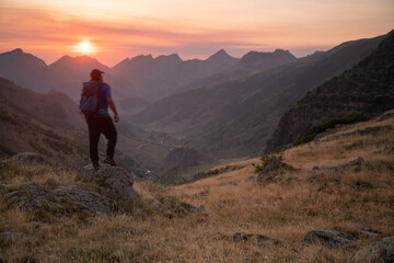 Fototapeta premium man standing on a mountain summit looking to the red sunset