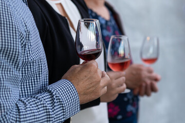 A man and two women hold a glass of red and rose wine in their hands.